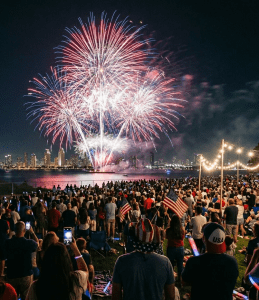 Large crowd watching colorful fireworks over city skyline at night during 4th of July celebration